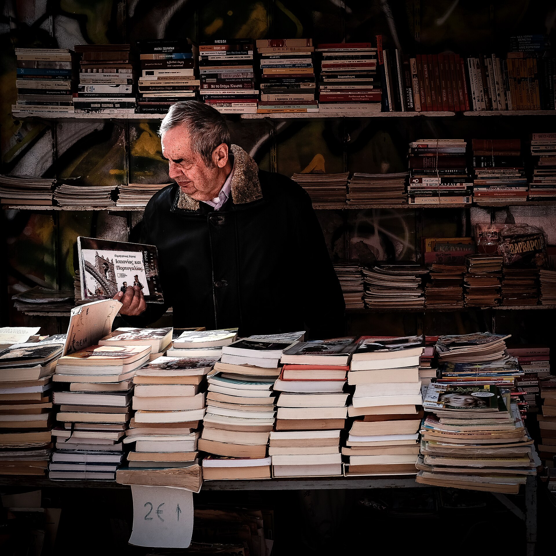 Читател разглежда книги пред плътно запълнени рафтове в атинска книжарница